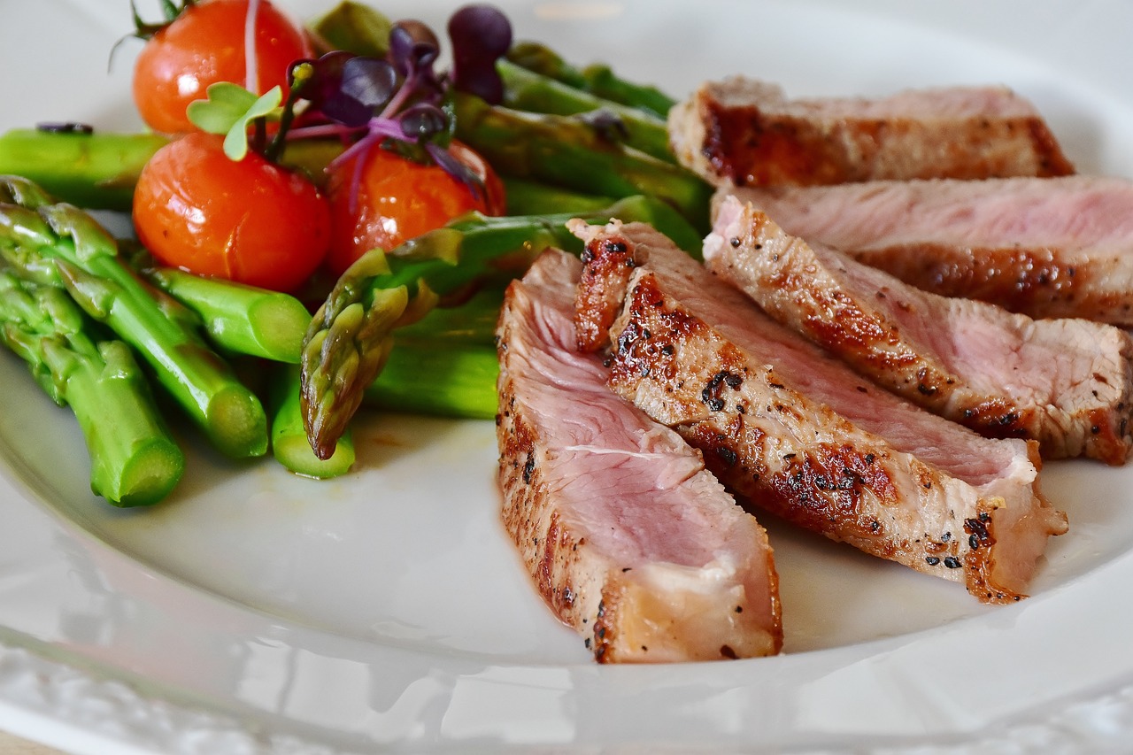 Grilled steak slices with asparagus and tomatoes on a plate.