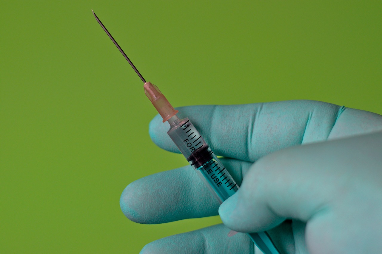 Gloved hand holding a medical syringe against a green backdrop.