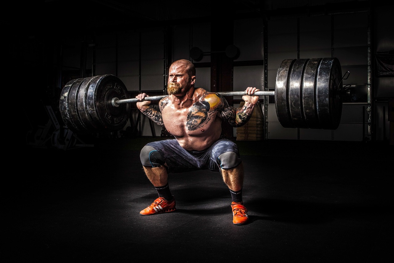 Muscular tattooed man doing a heavy barbell squat.